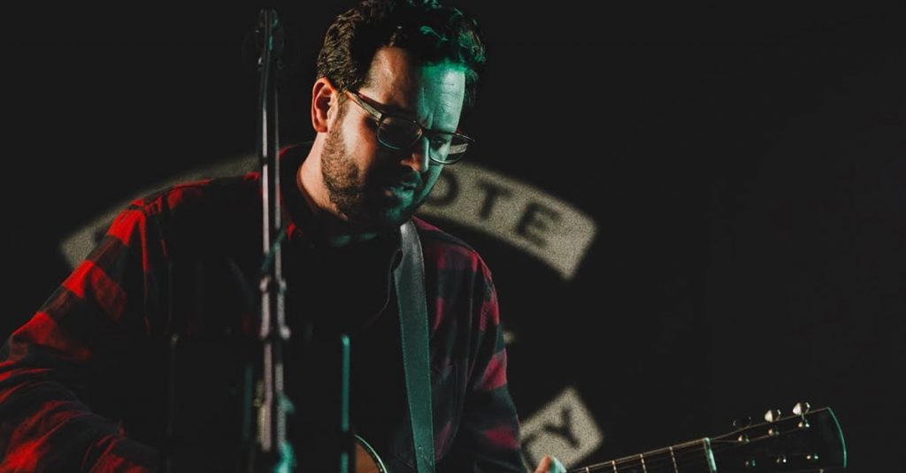 Bradley Kerr playing acoustic guitar on stage during a live performance.