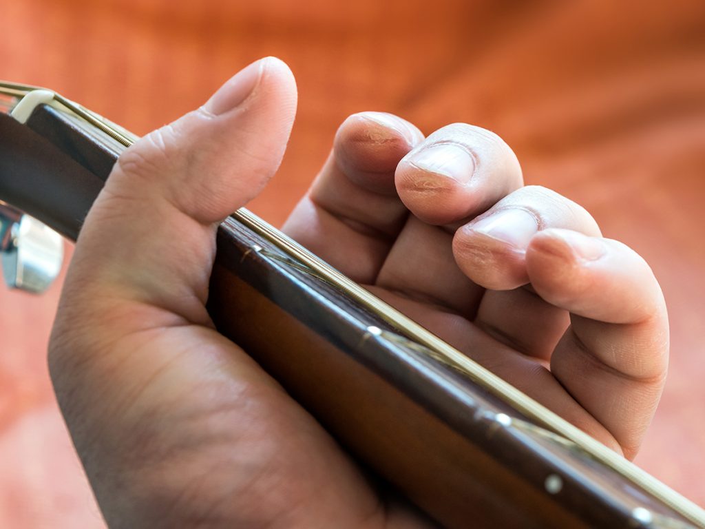 A close up image of sore guitar calluses on a guitar players fingers as they are holding the guitar neck. 
